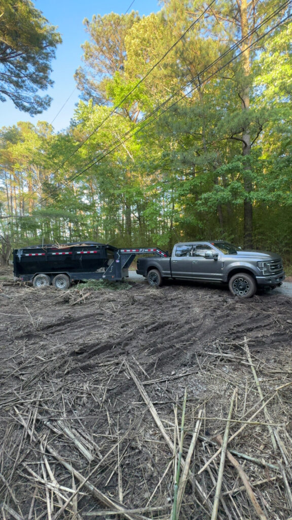 Truck towing a black dumpster in a wooded area, showcasing dumpster rental services for home renovations and cleanouts in Delmarva.